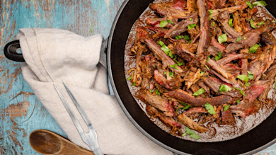 Shredded venison barbacoa in cast-iron skillet, garnished with cilantro