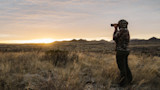 Hunter using binoculars at sunrise in camouflage on desert plains