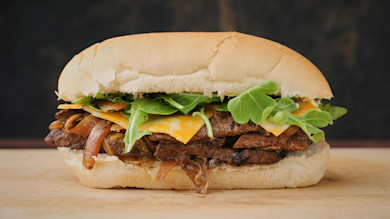 Steak sandwich on hoagie roll with cheddar, caramelized onions, and arugula