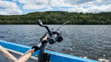 Spinning rod and reel on blue boat rail, lake with forested shoreline