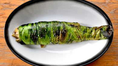 Trout wrapped in charred ramp leaves on white oval plate