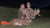Man and woman kneel behind a massive-antlered buck at night