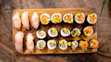 Wooden board with six white-fish nigiri and assorted maki rolls with avocado and spicy sauce; "Hawaii" on board