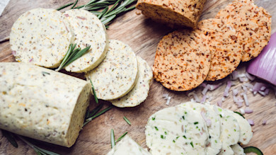Sliced compound butters with rosemary sprigs and chopped shallot on a wooden board