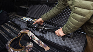 Hunter placing scoped bolt-action rifle into foam-lined hard case in truck bed