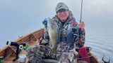 Man holding smallmouth bass in wooden rowboat on a foggy lake