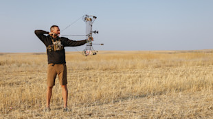 Man at full draw with compound bow in dry prairie