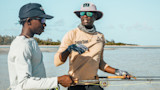 Fishing guide pointing, shirt reads "Captain Shawn", two men wading with fly rods