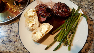 Rolled stuffed venison backstrap, pan sauce, sauteed asparagus and buttered baguette slices on plate