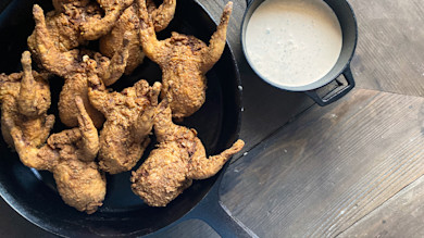 Pickle-fried quail in cast-iron skillet with cup of creamy dipping sauce on wooden table