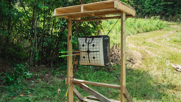 Wooden archery target stand with square target pierced by three green-fletched arrows