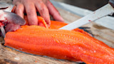 Salmon fillet being cut with bloodstained knife on wooden board, hand holding the fish