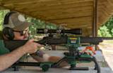 Shooter aiming rifle on CALDWELL LEAD SLED MAX at covered outdoor firing bench