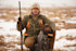 Hunter kneeling in snowy field with shotgun and hunting dog, jacket labeled Orvis