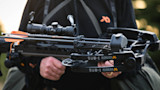 Crossbow with text 'SUB-1 MISSION CROSSBOWS' held by hunter wearing First Lite jacket with orange logo