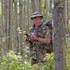 Hunter in aspen grove wearing camouflage, bucket hat and sunglasses, holding a phone