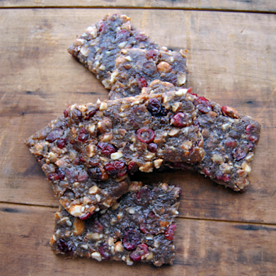 Three venison and cranberry snack bars with chopped nuts on a wooden board