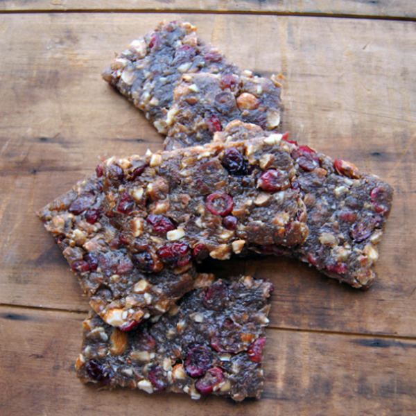 Three venison and cranberry snack bars with chopped nuts on a wooden board