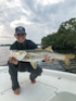 Woman holding large snook on boat, wearing cap reading 'DEEP BLUE YACHT DELIVERY'