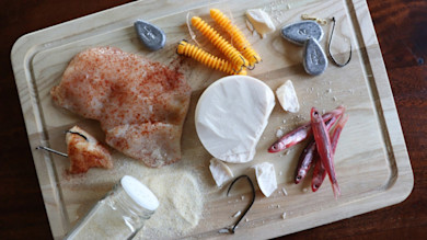 Cutting board with catfish baits: seasoned chicken, cheese disk, small red baitfish, plastic baits, sinkers, hooks