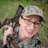 Smiling woman hunter wearing glasses and camo cap carrying a wild turkey over her shoulder
