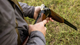 Hunter loading over-under shotgun with two shells, standing over grassy field