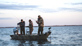 Three men fishing from a small boat at dawn, two casting rods and one holding a landing net