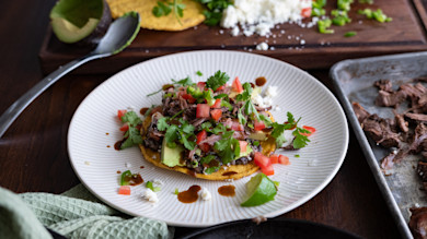 Turkey tostada with shredded turkey, black beans, avocado, diced tomato, cilantro, queso fresco, lime wedge