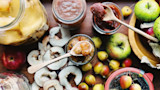 Jars of apple preserves with spoons, dried apple rings and fresh apples on a wooden board