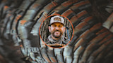 Hunter smiling in camo cap with patch "onX Hunt", circular inset over turkey feathers