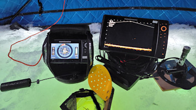 Two Humminbird fishfinder screens for ice fishing in blue shelter, sonar readings, yellow scoop