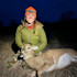 Hunter kneeling at night in orange beanie and headlamp, smiling while holding a harvested doe