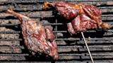 Two grilled meat pieces on a charred grill grate, one pierced by a metal skewer