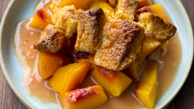 Peach cobbler with golden biscuit topping and peach chunks in syrup on white plate