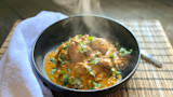 Steaming curry with meat and cilantro over rice in a black bowl
