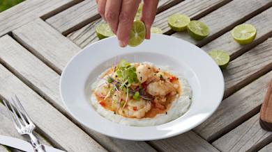 Hand squeezing lime over spiny lobster on coconut grits garnished with microgreens