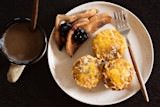 Three cheesy egg muffins on a plate with jam-topped toast triangles, fork, and mug of coffee