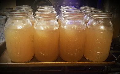 Mason jars of pale golden stock with metal lids on a baking sheet