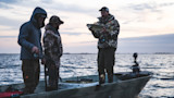 Man holding walleye on boat with two other men at dusk on lake