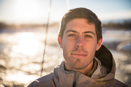 Man in hooded jacket facing camera with sunlit river bokeh behind him