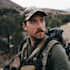 Hunter wearing camo YETI cap, mustache, backpack and binoculars in scrubland