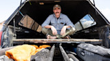 Ryan Callaghan seated cross-legged in pickup truck bed under camper shell; YETI bag visible