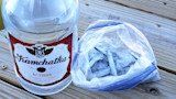 Bottle labeled Kamchatka 42 PROOF vodka beside zip-top bag of small frozen fish on wooden deck