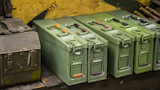Green metal ammunition boxes with latch handles and loose rifle cartridges on a shelf