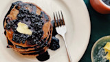 Stack of acorn pancakes topped with butter and dark berry syrup on a white plate