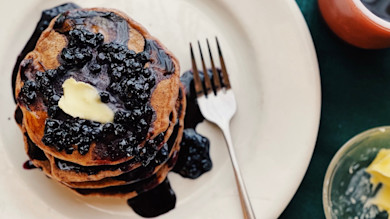 Stack of acorn pancakes topped with butter and dark berry syrup on a white plate
