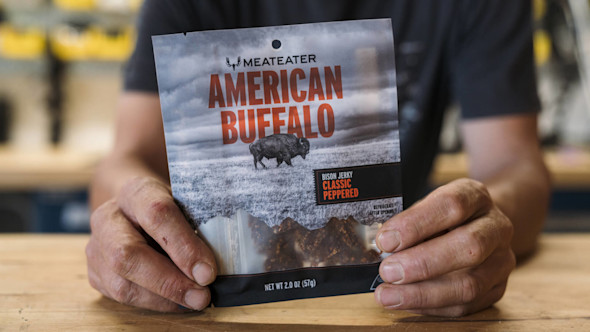 MeatEater "AMERICAN BUFFALO" bison jerky bag held by hands, label "Bison Jerky Classic Peppered"