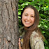 Smiling woman in camouflage shirt leaning against a tree with green leaves background