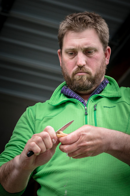 Man in green Patagonia jacket using a knife to cut a small food item, liquid dripping