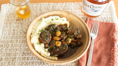 Venison medallions in gravy with onions over mashed potatoes; fork and bottle labeled Fox & Den